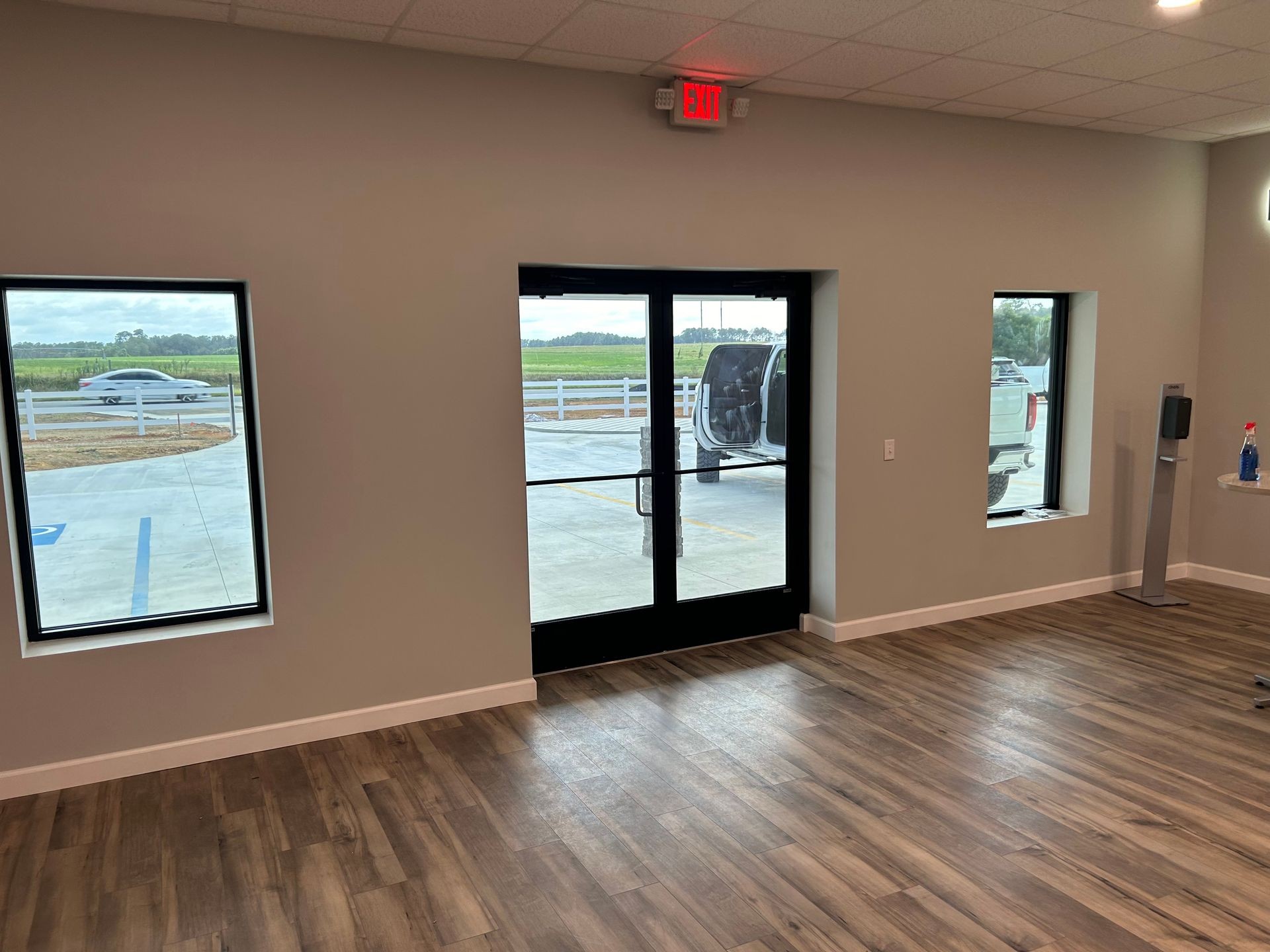 Interior of a room with wood flooring, large glass door, and windows showing parked vehicles outside.