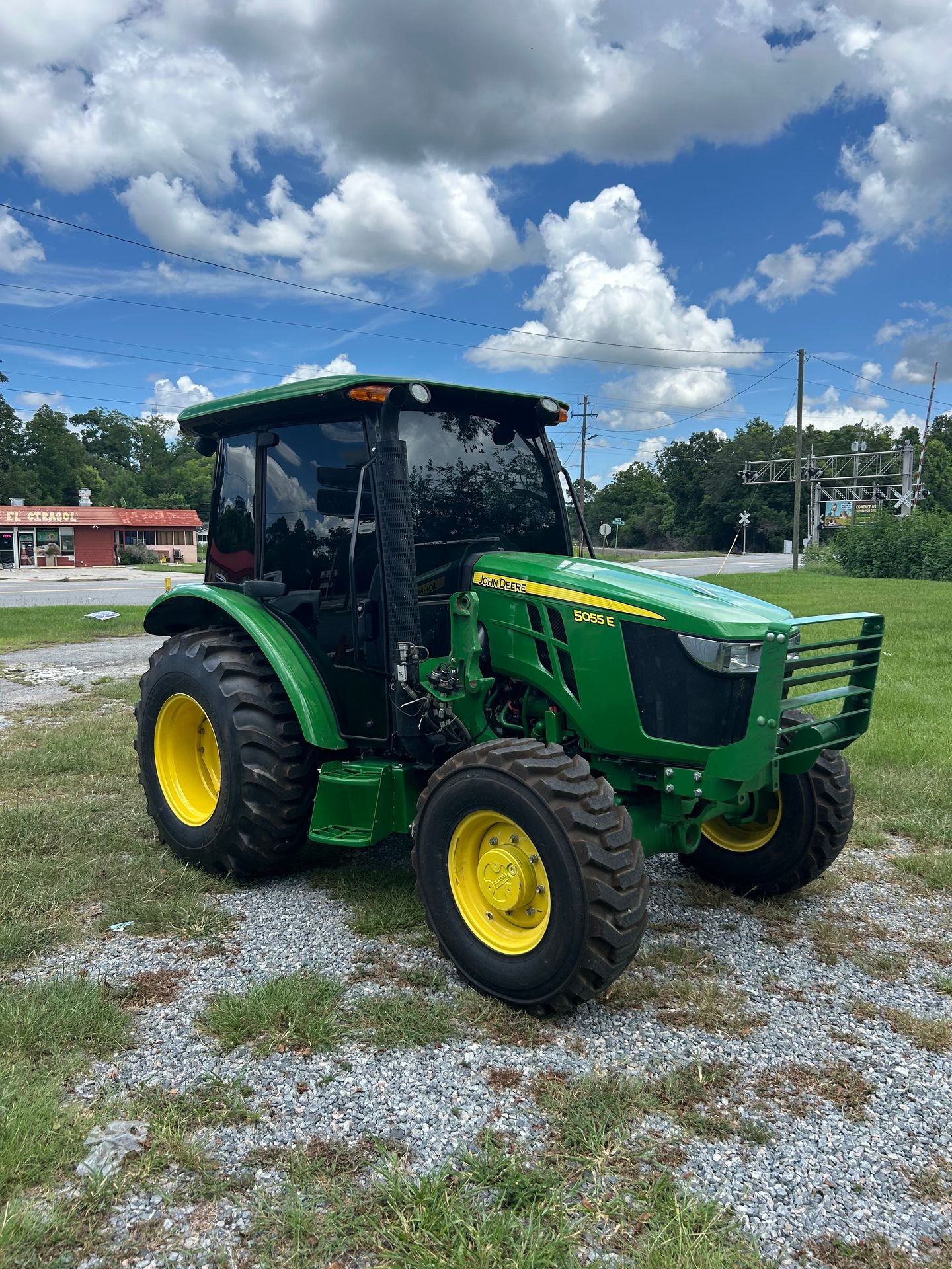Green tractor parked on gravel with a cloudy sky background.
