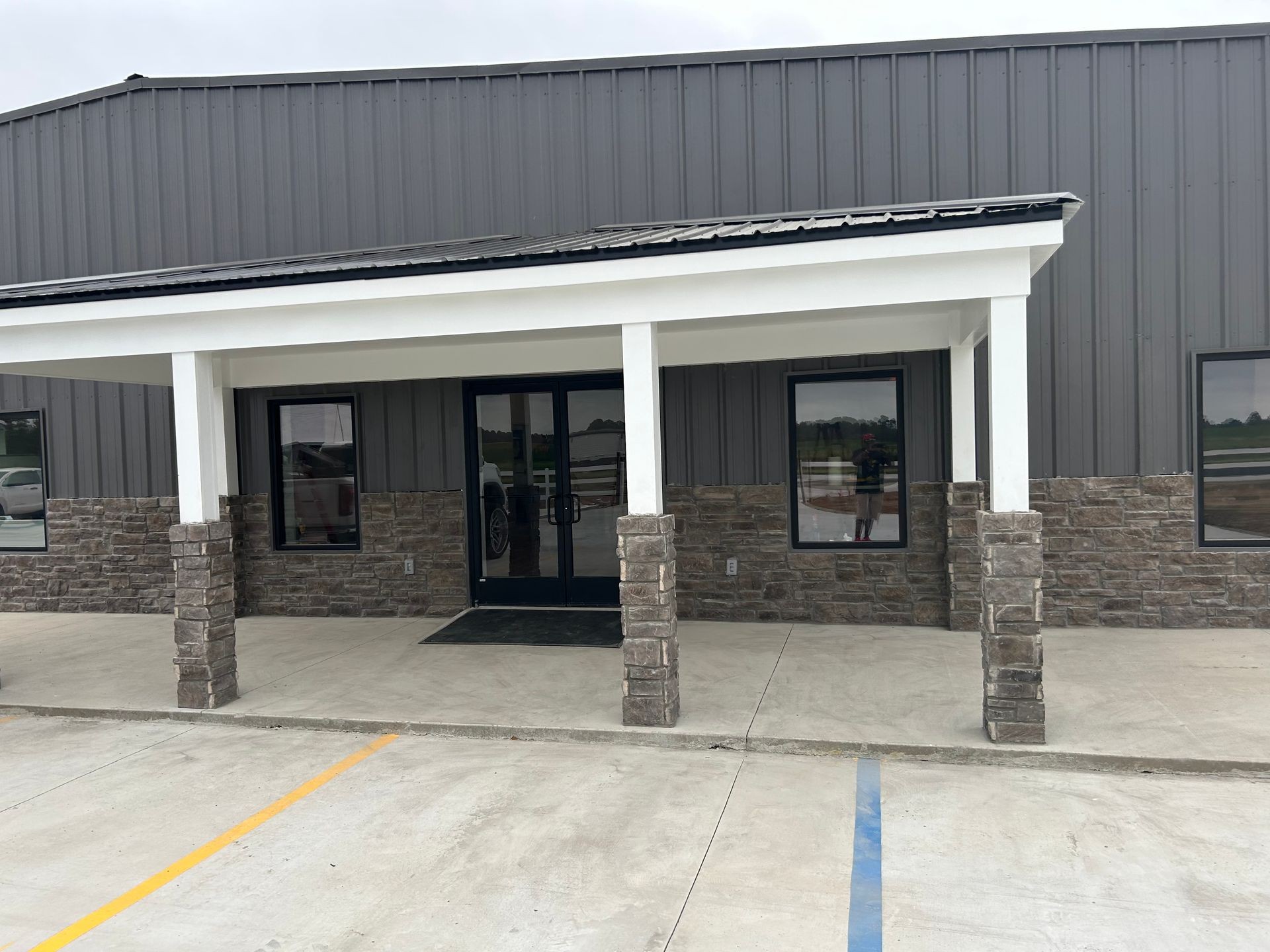 Exterior of a building with stone and metal siding, featuring a covered entrance with white columns.
